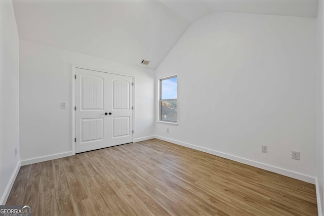 unfurnished bedroom with a closet, vaulted ceiling, and light wood-type flooring