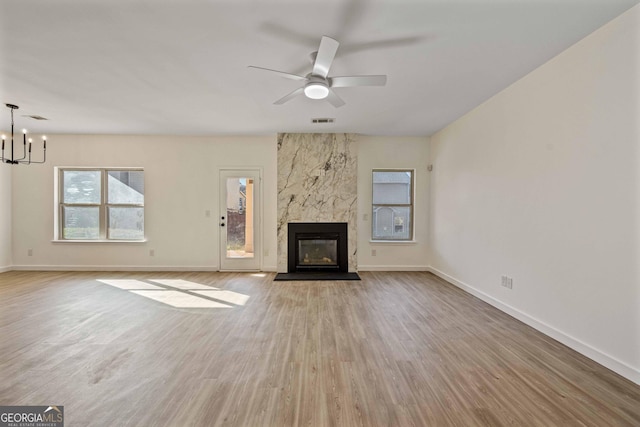 unfurnished living room featuring a high end fireplace, ceiling fan with notable chandelier, and light wood-type flooring