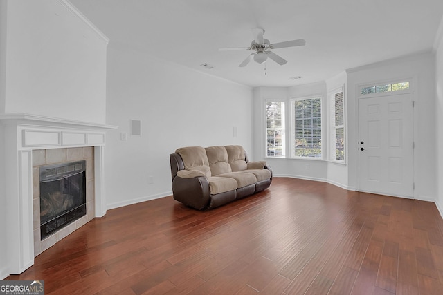 living room with dark hardwood / wood-style floors, ceiling fan, crown molding, and a tiled fireplace