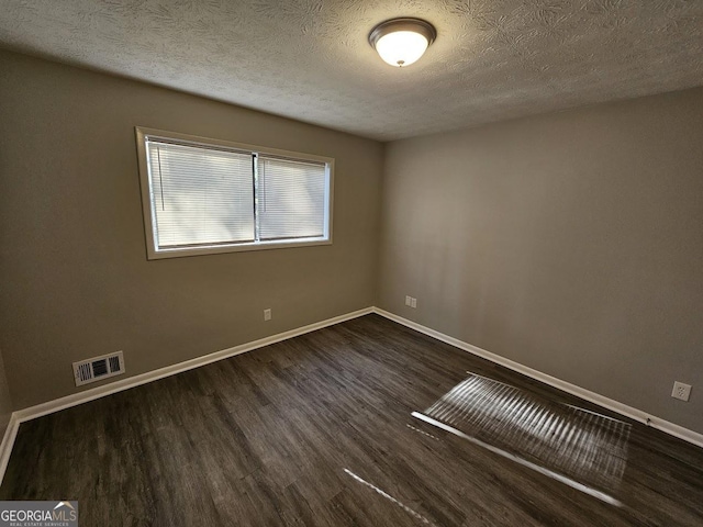 spare room featuring a textured ceiling and dark hardwood / wood-style flooring