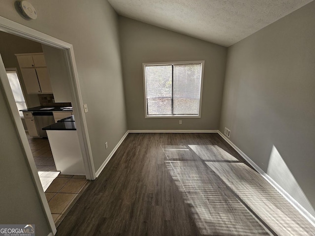 spare room featuring a textured ceiling, dark wood-type flooring, and vaulted ceiling