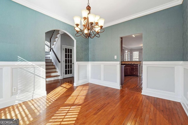 unfurnished dining area with hardwood / wood-style flooring, a notable chandelier, and ornamental molding