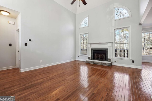 unfurnished living room with ceiling fan, a towering ceiling, and hardwood / wood-style flooring