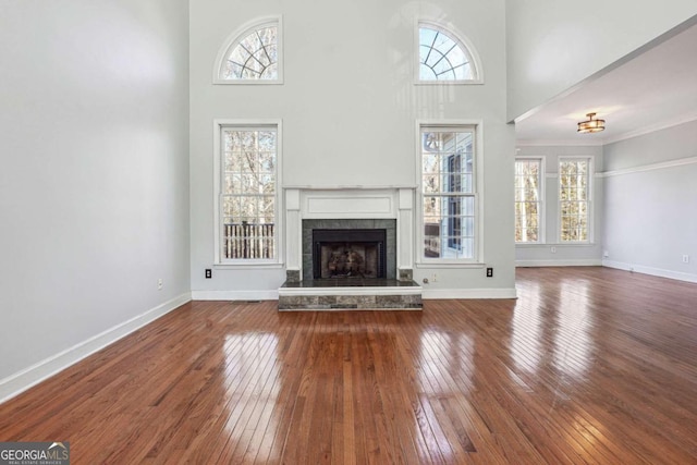 unfurnished living room featuring crown molding, plenty of natural light, a towering ceiling, and hardwood / wood-style floors