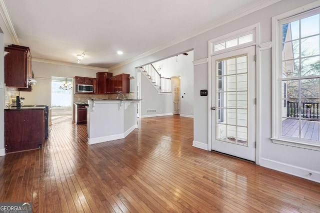 kitchen featuring dark hardwood / wood-style floors, stainless steel microwave, a kitchen bar, and crown molding