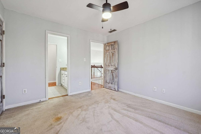 unfurnished bedroom featuring light colored carpet, ensuite bath, and ceiling fan