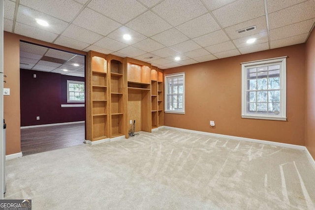 unfurnished living room with a drop ceiling, carpet, and a healthy amount of sunlight