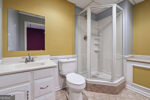 bathroom featuring a drop ceiling, vanity, a shower with shower door, and toilet