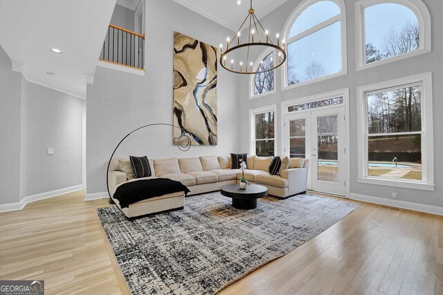 living room featuring a towering ceiling, light wood-type flooring, crown molding, and a notable chandelier