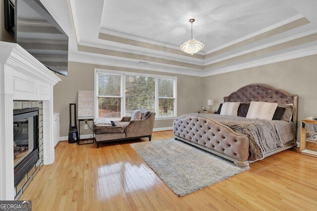 bedroom with a raised ceiling, crown molding, a notable chandelier, and light wood-type flooring