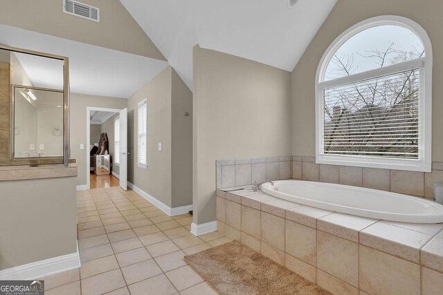 bathroom with tiled bath, a wealth of natural light, tile patterned flooring, and vaulted ceiling