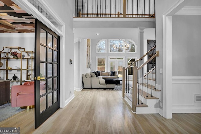 entryway featuring french doors, a towering ceiling, ornamental molding, light hardwood / wood-style flooring, and a chandelier