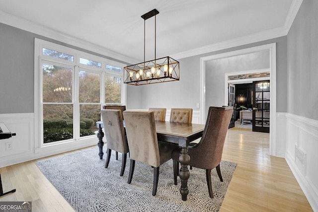 dining space with plenty of natural light, an inviting chandelier, ornamental molding, and light hardwood / wood-style flooring