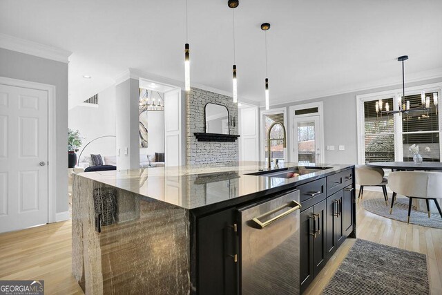 kitchen with sink, dark stone countertops, a large island with sink, decorative light fixtures, and light wood-type flooring