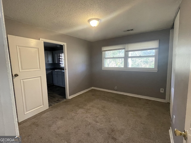 spare room featuring a textured ceiling and dark colored carpet