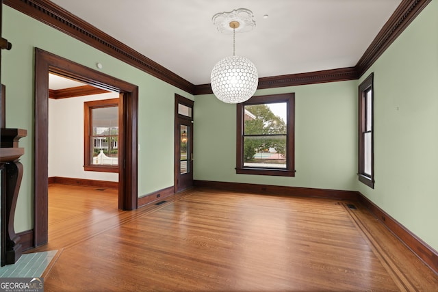 empty room featuring light hardwood / wood-style floors, crown molding, and a notable chandelier