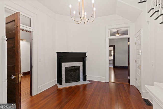 unfurnished living room with ceiling fan with notable chandelier, vaulted ceiling, dark hardwood / wood-style flooring, and a brick fireplace