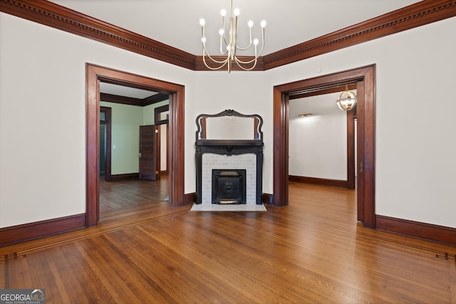 unfurnished living room with crown molding, a fireplace, a notable chandelier, and hardwood / wood-style flooring