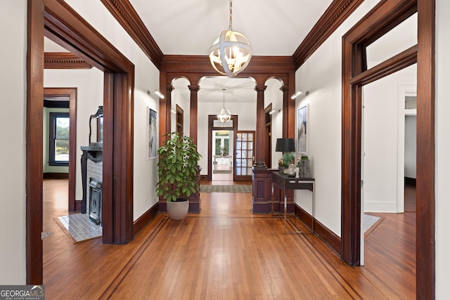 hall with french doors, decorative columns, ornamental molding, a chandelier, and hardwood / wood-style floors