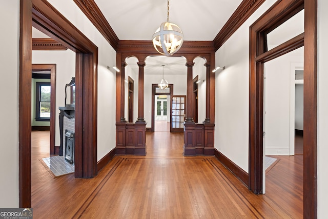 hall with ornate columns, crown molding, dark wood-type flooring, and a notable chandelier