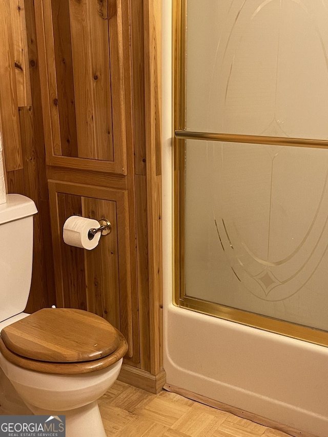 bathroom featuring toilet, parquet floors, and enclosed tub / shower combo