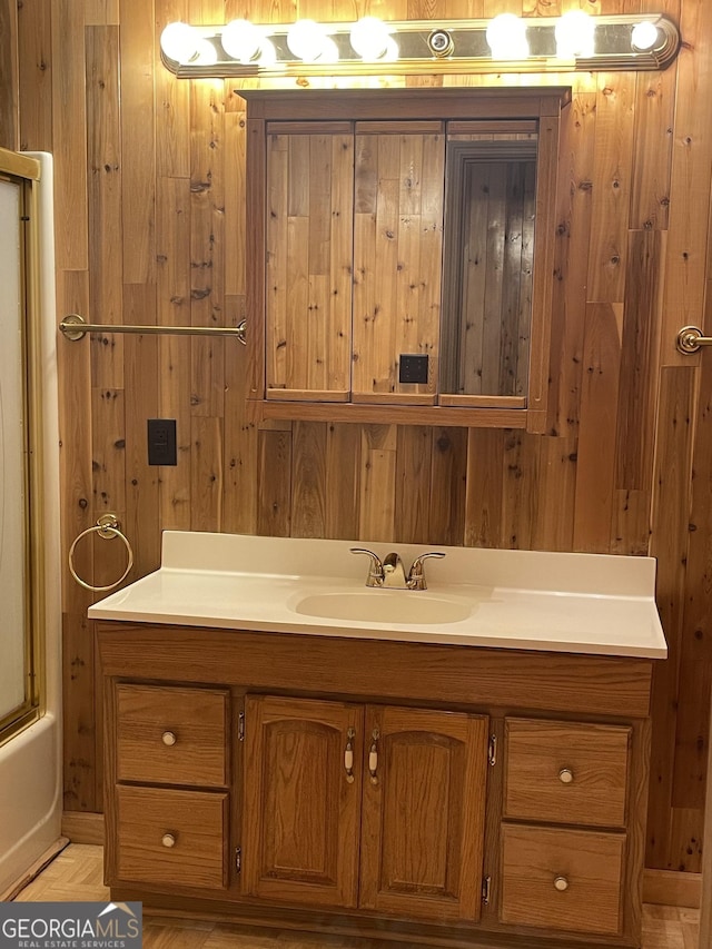 bathroom with vanity, wood walls, and bath / shower combo with glass door