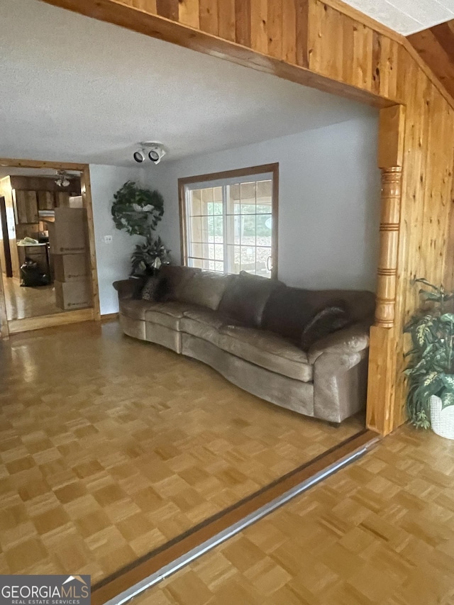 unfurnished living room with parquet floors, a textured ceiling, and wooden walls