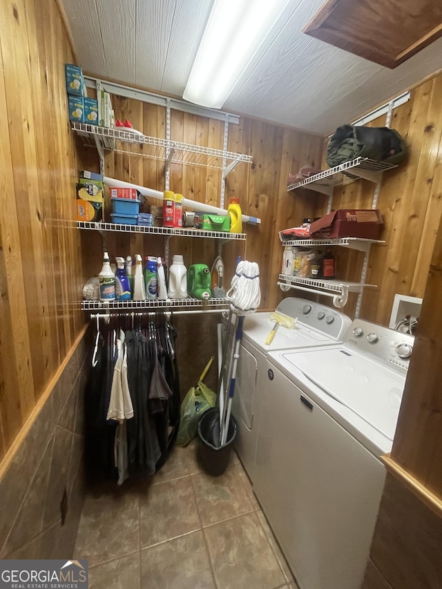 clothes washing area with tile patterned flooring, wood walls, and independent washer and dryer