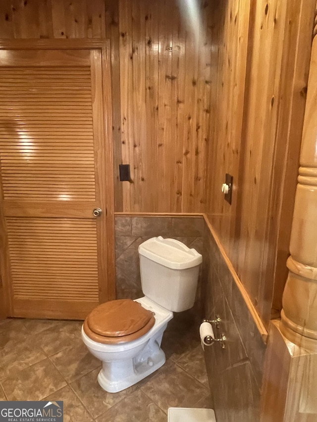 bathroom featuring tile patterned floors, wood walls, toilet, and tile walls