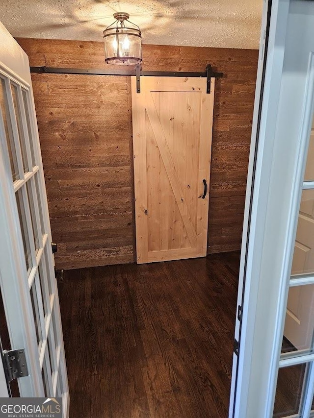 interior space featuring a barn door, wooden walls, dark wood-type flooring, and a textured ceiling