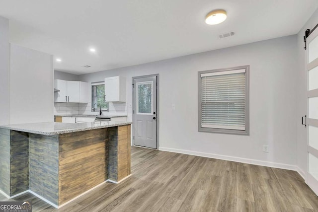 kitchen featuring white cabinets, sink, a barn door, light stone counters, and kitchen peninsula