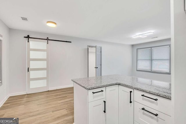 kitchen with a barn door, light stone counters, white cabinetry, and light wood-type flooring