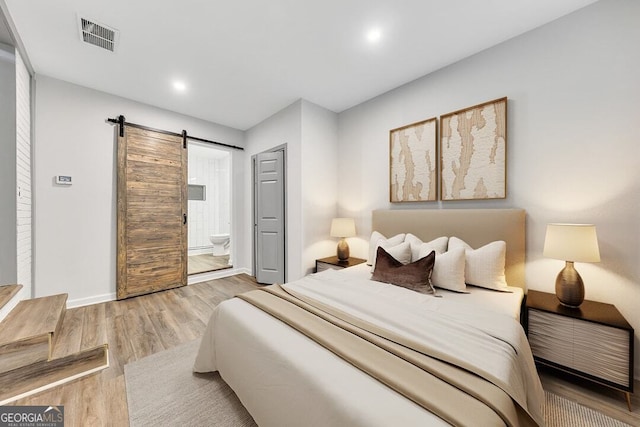 bedroom featuring hardwood / wood-style floors, a barn door, and ensuite bathroom