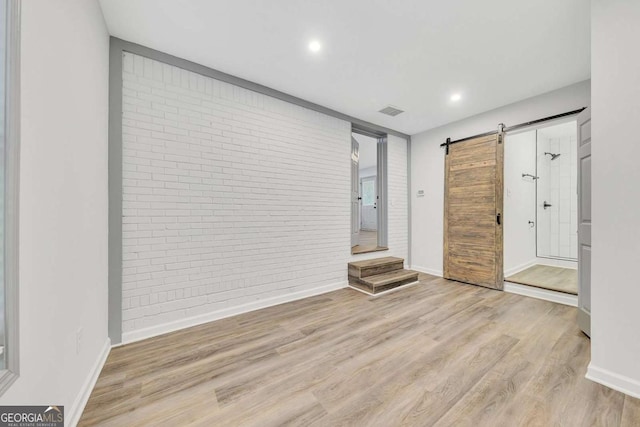 entrance foyer with a barn door, brick wall, and light hardwood / wood-style floors