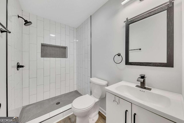 bathroom featuring vanity, toilet, wood-type flooring, and tiled shower