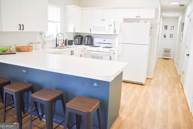 kitchen featuring white appliances, a kitchen breakfast bar, sink, kitchen peninsula, and white cabinetry