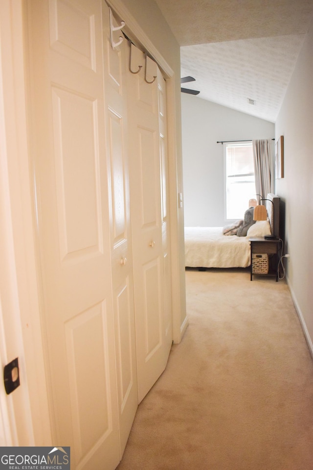 corridor with a textured ceiling, light colored carpet, and vaulted ceiling