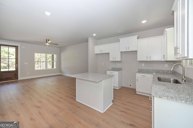 kitchen with sink, white cabinetry, light stone counters, a center island, and light hardwood / wood-style flooring