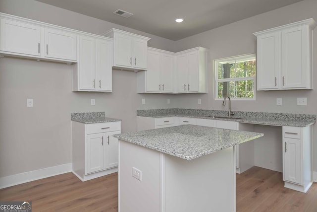 kitchen featuring sink, white cabinetry, light stone counters, a center island, and light hardwood / wood-style floors