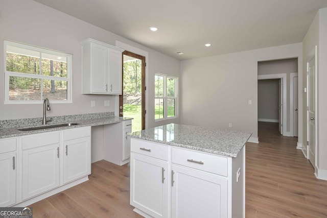 kitchen with sink, light stone counters, a center island, light wood-type flooring, and white cabinets