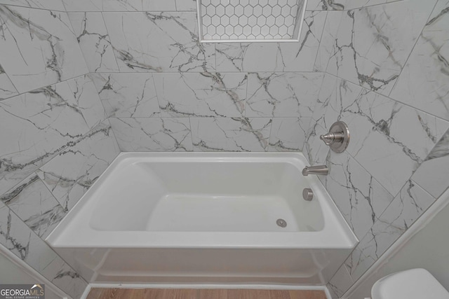 bathroom with tiled shower / bath combo and toilet