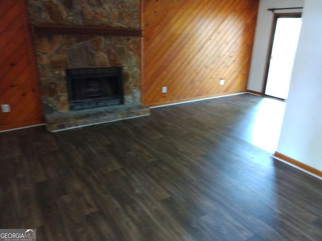 unfurnished living room featuring wooden walls, a fireplace, and dark wood-type flooring