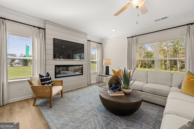 living room featuring ceiling fan, a large fireplace, ornamental molding, and light hardwood / wood-style flooring