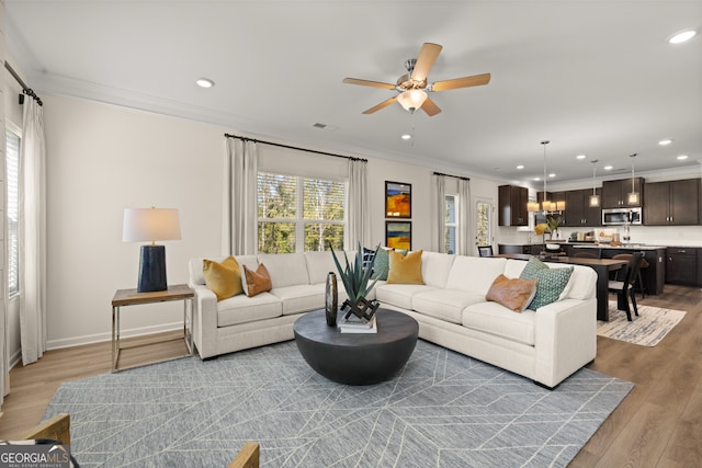 living room featuring light hardwood / wood-style flooring, ceiling fan, and crown molding