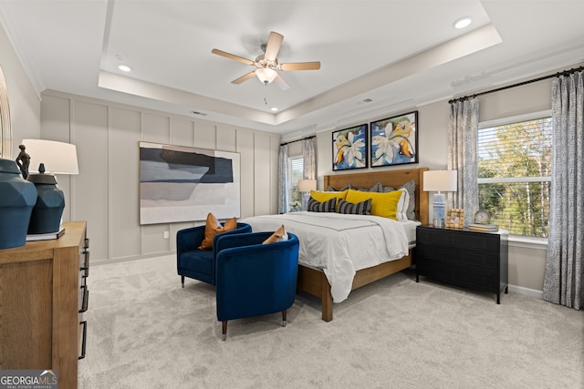 carpeted bedroom with a tray ceiling, ceiling fan, and ornamental molding