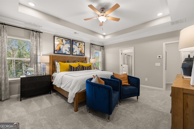 carpeted bedroom featuring a tray ceiling, ceiling fan, and ensuite bathroom