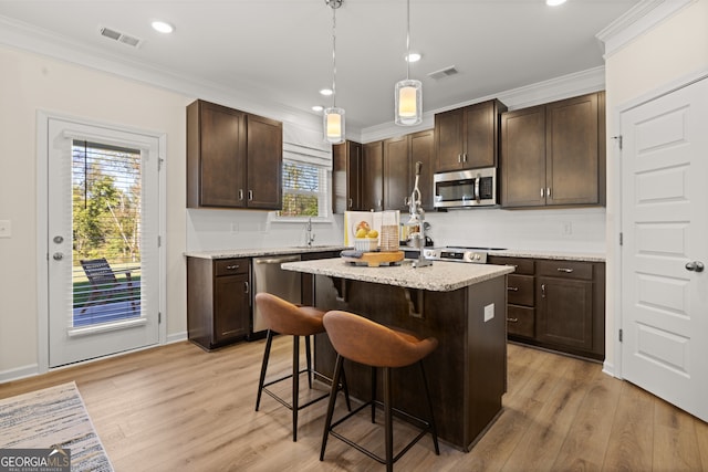 kitchen with dark brown cabinetry, a center island, stainless steel appliances, light hardwood / wood-style flooring, and a breakfast bar area