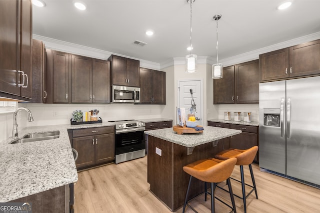 kitchen with a breakfast bar, sink, light hardwood / wood-style flooring, appliances with stainless steel finishes, and a kitchen island