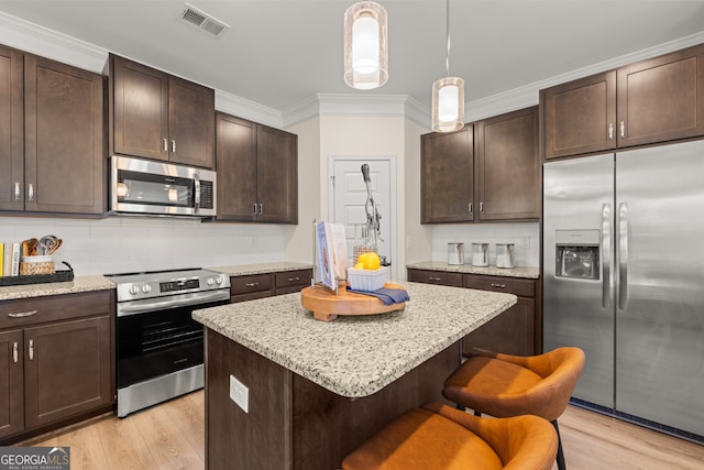 kitchen featuring appliances with stainless steel finishes, light wood-type flooring, a center island, and dark brown cabinets