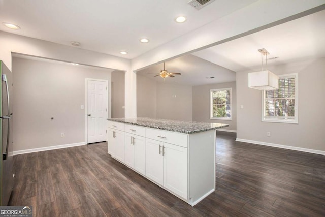 kitchen with white cabinetry, dark wood-type flooring, light stone counters, decorative light fixtures, and a kitchen island